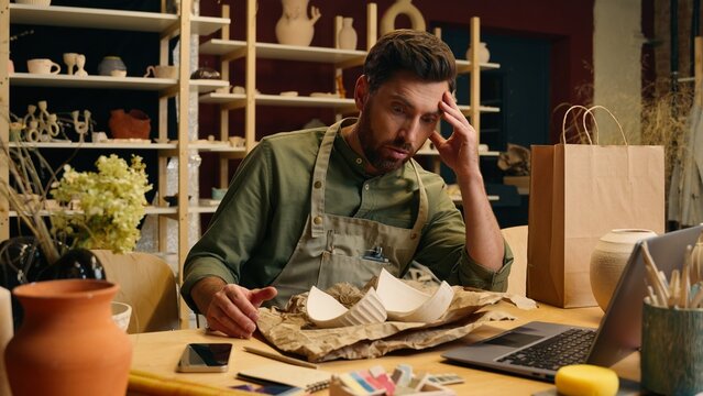Sad upset Caucasian man guy small business owner craftsman businessman male record video online unboxing laptop accidentally broke pottery shatter ceramic crockery packaging shopping indoors workshop - Powered by Adobe
