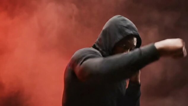 Intense hooded fighter shadowboxing in dramatic red smoke background scene