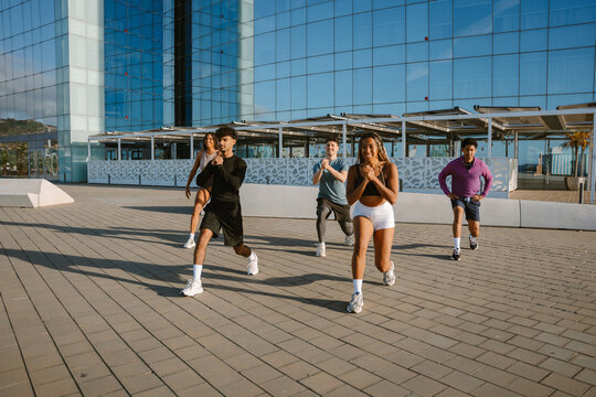 A group of five athletes lunge and smile while three of them hold their hands together in front of them
