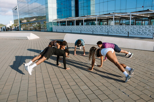 A group of five athletes stand in a circle and rest their hands on the ground