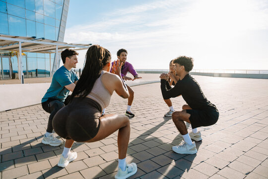A group of five athletes squat in a circle and hold their hands together in front of them while two of them laugh