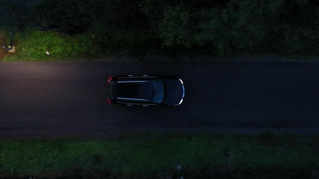 Aerial drone view of a black car on road at night