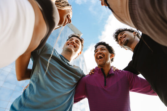 A group of five athletes stand in a circle and laugh while hugging each other - Powered by Adobe