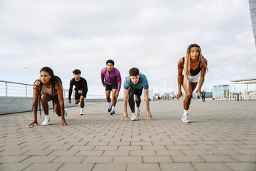 A female and male athlete stand in starting positions while a group of three athletes run next to them