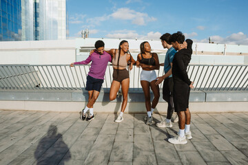 A group of five athletes stand and talk while four of them lean on the fence and two of them laugh and hug each other