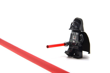 Fototapeta premium Lego minifigure of Darth Vader from Star Wars with lightning sword is staying before red line isolated on white. Editorial illustrative image of stop war idea.