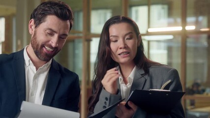 Multiethnic cheerful business colleagues laughing reviewing documents Korean woman professional Caucasian man partner teamwork clipboard analysis office success planning cooperation report strategy - Powered by Adobe