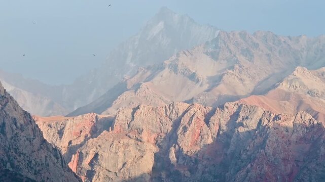 Birds fly above Iskanderkul, also known as Alexander Lake, in the Fann Mountains of Tajikistan, with rugged peaks, calm water, and remote Central Asia alpine scenery.