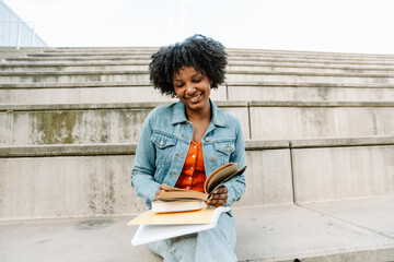 Female student smiling and reading a book while sitting on the bleachers