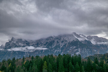 Snowy alpine mountains with forest and low clouds in misty autumn weather