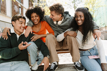 A group of four students hug and laugh while talking and sitting on a table and bench