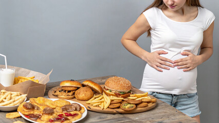 junk food eating too much concept Woman holds her stomach near a table full of fast food in a casual setting during daytime