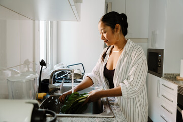 Woman standing and washing greens in sink with tap water