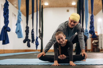 Man is teaching. Male instructor assisting a child during yoga practice in a fitness studio