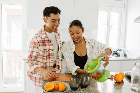Woman pouring juice from juicer into glasses while standing at table next to man and they are smiling