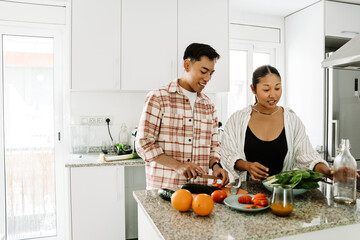 A man is cutting vegetables and talking to a woman who is taking a bottle while they are standing at the table