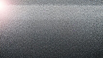 Abstract close-up of dark textured surface with bright lens flare and fine particles