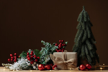 Gift box, fir tree and Christmas ornaments over brown background with copy space. Festive winter holiday backdrop. Design for banner or greeting card