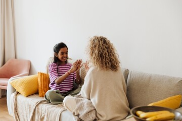 Daughter laughs and applauds while sitting on the couch across from her mother