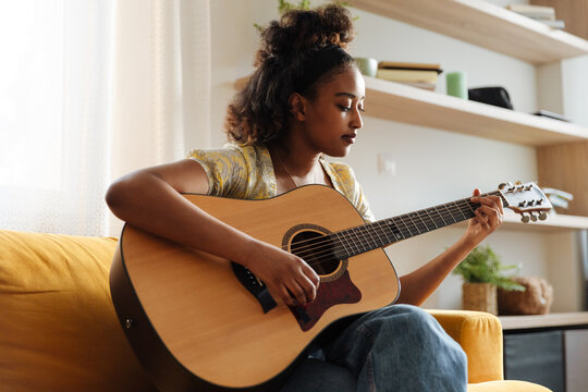 Female musician holding a guitar and playing it while sitting on a couch