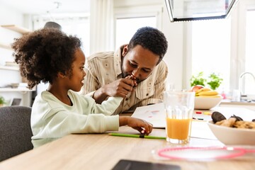 A father kisses the hand of his smiling daughter as they sit at the table