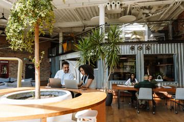 Male and female workers looking at laptop and sitting at table while he laughs and holds pencil