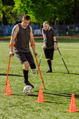 Obraz premium A man on crutches dribbles a ball between cones while a man on crutches looks on