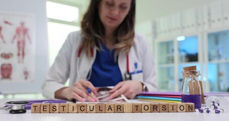 Wooden blocks spell words Testicular Torsion while woman urologist studies notebook. Female doctor writes plan explaining testicular torsion pain