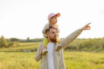 Father carrying toddler on his shoulders while pointing into the distance at sunset. Warm natural light, joyful family moment and outdoor exploration.