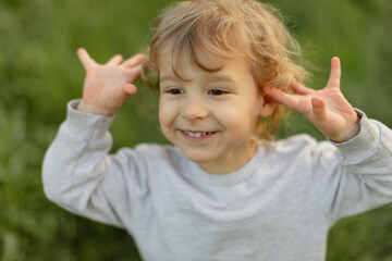 Joyful toddler making a playful gesture outdoors, smiling and having fun in a green field during warm natural light.