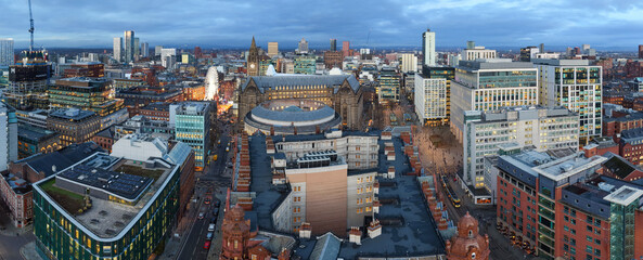 Panoramic aerial view of Manchester at dusk, showing a wide winter skyline with glowing lights and vibrant festive city atmosphere.