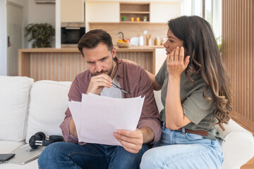Worried couple reviewing bills and startup financial report, planning tax payments, discussing budget challenges and searching solutions together for money management during economic uncertainty