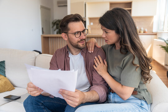 Worried couple reviewing bills and startup financial report, planning tax payments, discussing budget challenges and searching solutions together for money management during economic uncertainty - Powered by Adobe