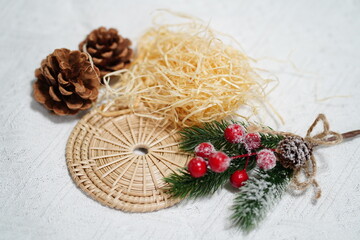 Natural elements arranged on a textured background, featuring pine cones, straw, festive red berries, green foliage, and a woven decorative mat