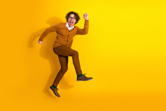 Happy young man with glasses jumps in a bright yellow studio setting wearing a cardigan and casual fashion