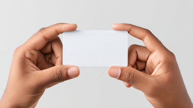Hands of an African American individual holding a blank business card against a neutral background, showcasing a clean and professional presentation for branding purposes