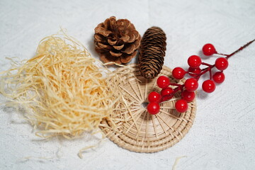 Natural elements featuring pine cones, red berries, wicker basket, and straw on textured background for decorative and artistic purposes