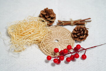 Natural Decorative Elements for Rustic Crafts Featuring Pinecones, Straw, Rattan Mat, Cinnamon Sticks, and Red Berries on White Background