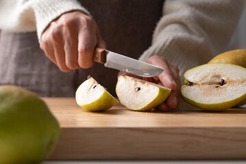 Hand holding kitchen knife and cutting pear on wooden board
