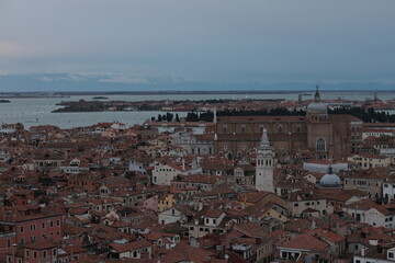 Obraz premium Panoramic view of Venice, Italy, with terracotta rooftops, historic churches, and a large basilica near the lagoon under a cloudy evening sky.