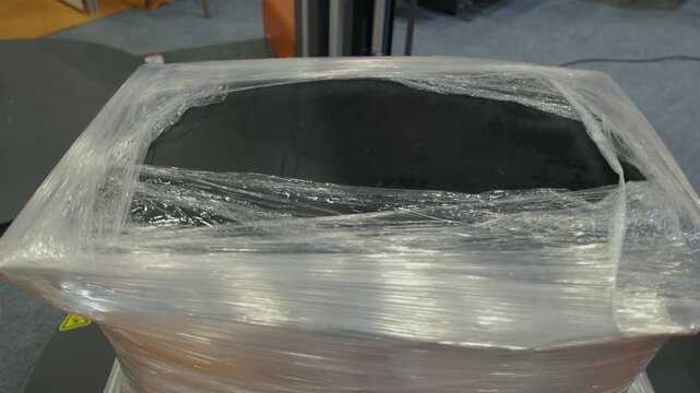 Top view of an industrial stretch wrapping machine securing a load with plastic film. Automated packaging process used in logistics, warehousing, and manufacturing operations.