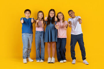 Preteen children standing in a row giving thumbs up in bright studio background. Confident and cheerful children expressing approval, unity and a positive school lifestyle mood
