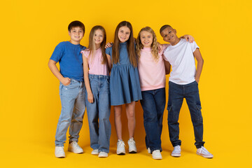 Fototapeta premium Preteen pupils standing close together and posing confidently in yellow studio background. A friendly group of children showing unity, friendship and a modern school lifestyle mood