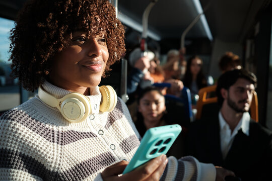 Young woman commuting on bus using smartphone and headphones - Powered by Adobe