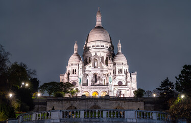 Illuminated Sacre-Coeur Basilica stands on Montmartre hill in Paris, France. Historic white stone church features large dome and Roman-Byzantine architecture in Ile-de-France region