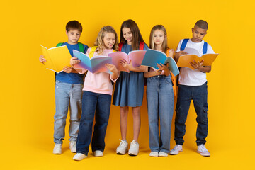 Fototapeta premium Preteen pupils reading colorful books together in a bright studio background. A friendly group of children focused on learning in a cheerful school lifestyle environ