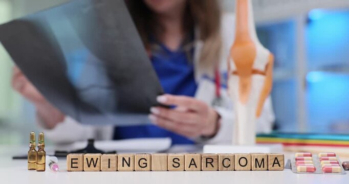 Ewing Sarcoma phrase on wooden cubes by medications and doctor holds limb x-ray image in clinic. Rare cancerous tumors in bones and soft tissues