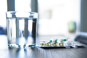 Pills, supplements, and a glass of water on the table.