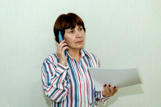 Senior woman discussing printed agreement via mobile phone, thoughtful expression.
