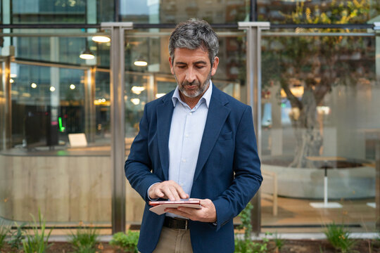 Mature businessman using tablet standing outside office building